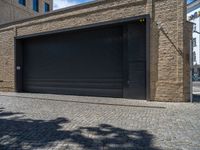 two windows in the side of a brick building, with a black garage door and brown door