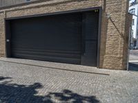 two windows in the side of a brick building, with a black garage door and brown door