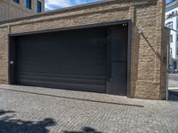 two windows in the side of a brick building, with a black garage door and brown door