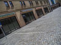 the sidewalk is paved with stones and has a bench in front of it, with no people inside