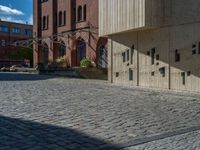 cobblestone driveway surrounded by modern buildings on sunny day with sun reflecting onto the windows