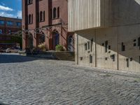 cobblestone driveway surrounded by modern buildings on sunny day with sun reflecting onto the windows