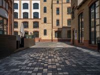 a sidewalk with chairs next to the brick building on the side, some have stairs and some buildings in the background