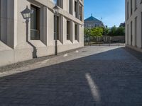 two people walking down an empty city street in an alley area with tall buildings in the background