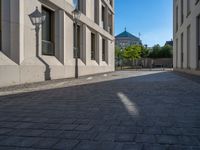 two people walking down an empty city street in an alley area with tall buildings in the background