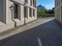 two people walking down an empty city street in an alley area with tall buildings in the background