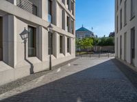 two people walking down an empty city street in an alley area with tall buildings in the background