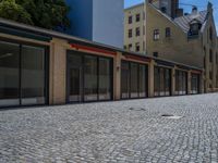 the sidewalk is paved with stones and has a bench in front of it, with no people inside