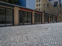 the sidewalk is paved with stones and has a bench in front of it, with no people inside