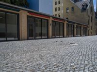 the sidewalk is paved with stones and has a bench in front of it, with no people inside