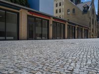 the sidewalk is paved with stones and has a bench in front of it, with no people inside