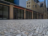 the sidewalk is paved with stones and has a bench in front of it, with no people inside