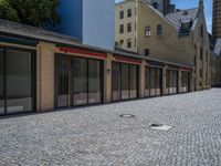 the sidewalk is paved with stones and has a bench in front of it, with no people inside