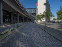 a cobble - stone road in front of an elevated bridge and building on the left, there is no traffic on the side