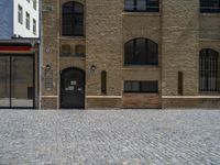 the sidewalk is paved with stones and has a bench in front of it, with no people inside