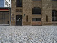 the sidewalk is paved with stones and has a bench in front of it, with no people inside