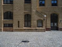 the sidewalk is paved with stones and has a bench in front of it, with no people inside