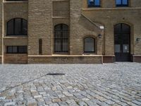 the sidewalk is paved with stones and has a bench in front of it, with no people inside