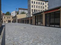 the sidewalk is paved with stones and has a bench in front of it, with no people inside