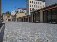 the sidewalk is paved with stones and has a bench in front of it, with no people inside