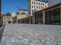 the sidewalk is paved with stones and has a bench in front of it, with no people inside