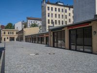 the sidewalk is paved with stones and has a bench in front of it, with no people inside