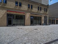 the sidewalk is paved with stones and has a bench in front of it, with no people inside