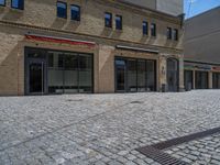 the sidewalk is paved with stones and has a bench in front of it, with no people inside