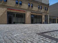 the sidewalk is paved with stones and has a bench in front of it, with no people inside