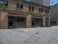 the sidewalk is paved with stones and has a bench in front of it, with no people inside