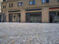 the sidewalk is paved with stones and has a bench in front of it, with no people inside