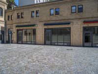 the sidewalk is paved with stones and has a bench in front of it, with no people inside