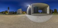 a panoramic view shows a walkway in front of buildings at night with a moon