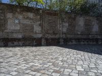 a view of a bricked concrete surface near a brick wall and trees in the background