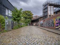 a brick road covered in graffiti next to buildings and greenery by the river bank