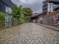 a brick road covered in graffiti next to buildings and greenery by the river bank