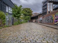 a brick road covered in graffiti next to buildings and greenery by the river bank