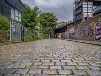 a brick road covered in graffiti next to buildings and greenery by the river bank