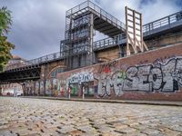 a brick road covered in graffiti next to buildings and greenery by the river bank