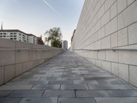 a long wall next to some buildings and water pipes on the sidewalk, some trees and the sky