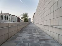 a long wall next to some buildings and water pipes on the sidewalk, some trees and the sky