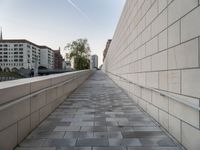 a long wall next to some buildings and water pipes on the sidewalk, some trees and the sky