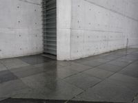 a skateboard on a sidewalk next to a building with a wall behind it on a rainy day