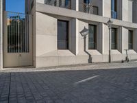 two people walking down an empty city street in an alley area with tall buildings in the background