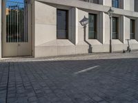 two people walking down an empty city street in an alley area with tall buildings in the background