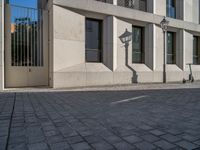 two people walking down an empty city street in an alley area with tall buildings in the background