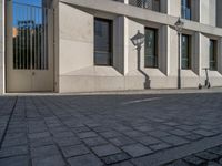 two people walking down an empty city street in an alley area with tall buildings in the background