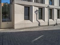 two people walking down an empty city street in an alley area with tall buildings in the background