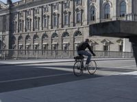 a man rides his bike past a large building on a sidewalk in front of an urban area