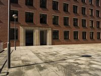 an empty courtyard that is near a brick building and several windows has a street sign on the sidewalk